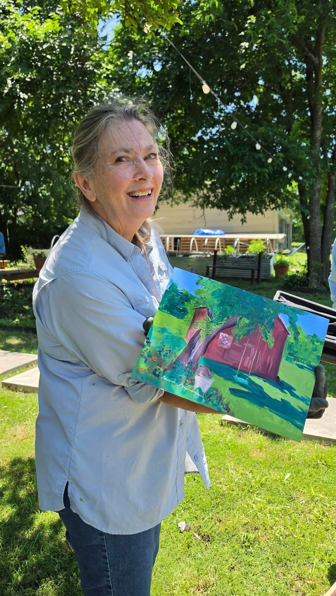 Artist holding a finished red barn painting inspired by the Four Winds grounds in Bonham Texas