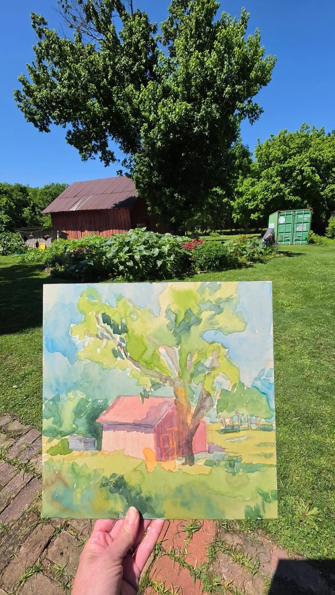 Finished watercolor painting shown in front of the Four Winds garden and red barn
